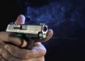 Pistola compacta disparando com mira laser verde acesa, feixe visível na fumaça — foto: Viridian Weapon Technologies