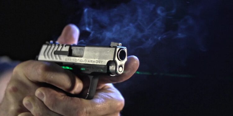 Pistola compacta disparando com mira laser verde acesa, feixe visível na fumaça — foto: Viridian Weapon Technologies