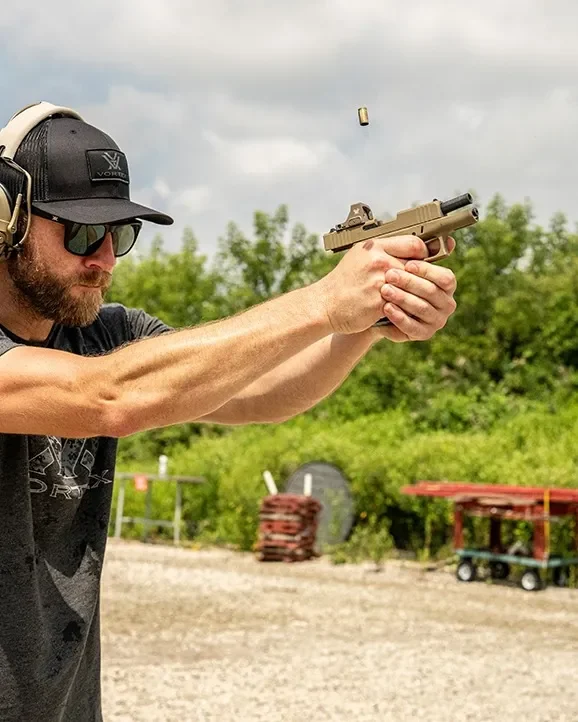 Atirador no estande disparando pistola com o red dot Vortex Defender-CCW Tan