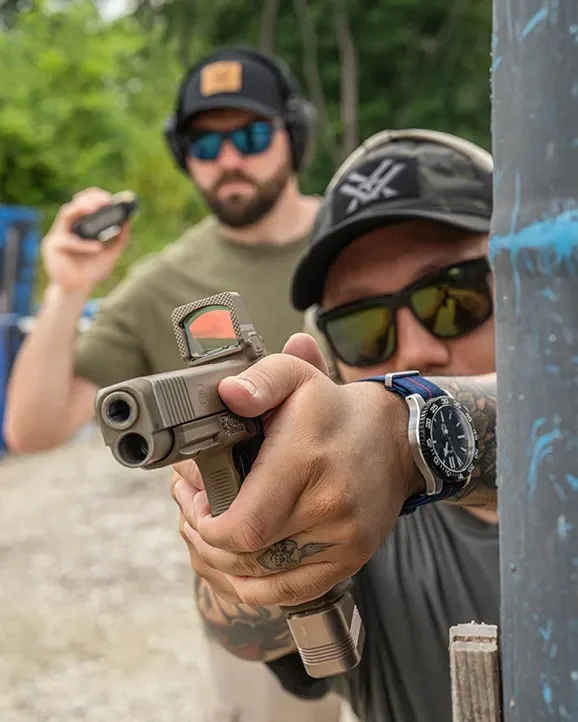 Atirador mirando pistola com o red dot Vortex Defender-XL Tan atrás de barricada